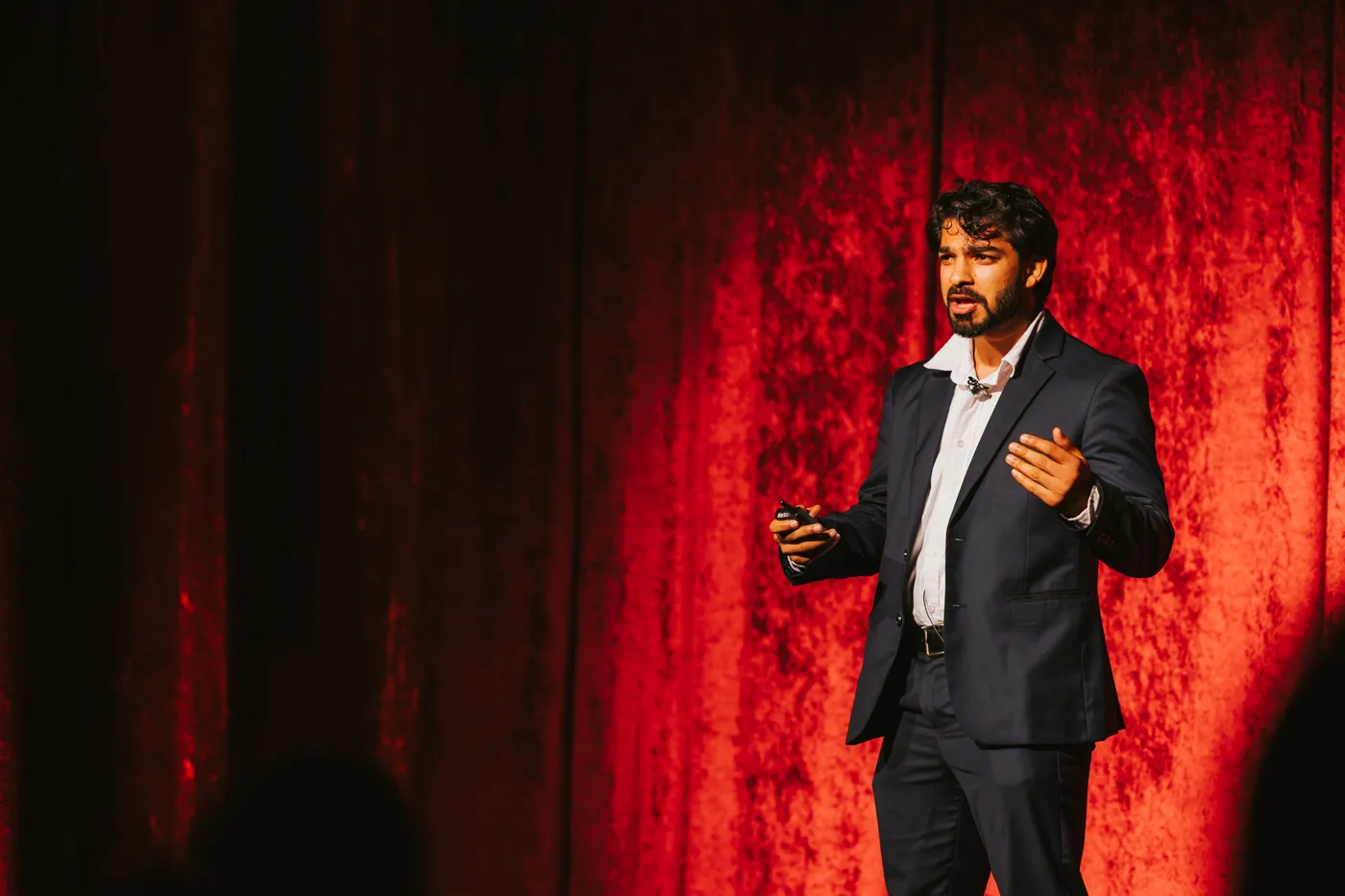 Aditya Goyal presenting on stage in front of a red curtain
